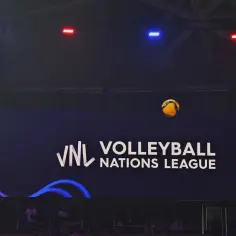 Piłka w locie nad boiskiem podczas meczu **liga narodów w siatkówce**. Na ekranie logo VNL Volleyball Nations League.