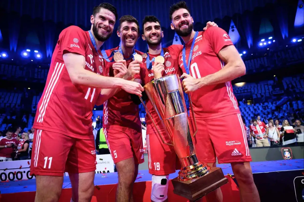 Siatkarze w czerwonych strojach z pucharem i medalami. Polska drużyna świętuje zwycięstwo, co z pewnością odzwierciedli mistrzostwa świata siatkówka tabela.